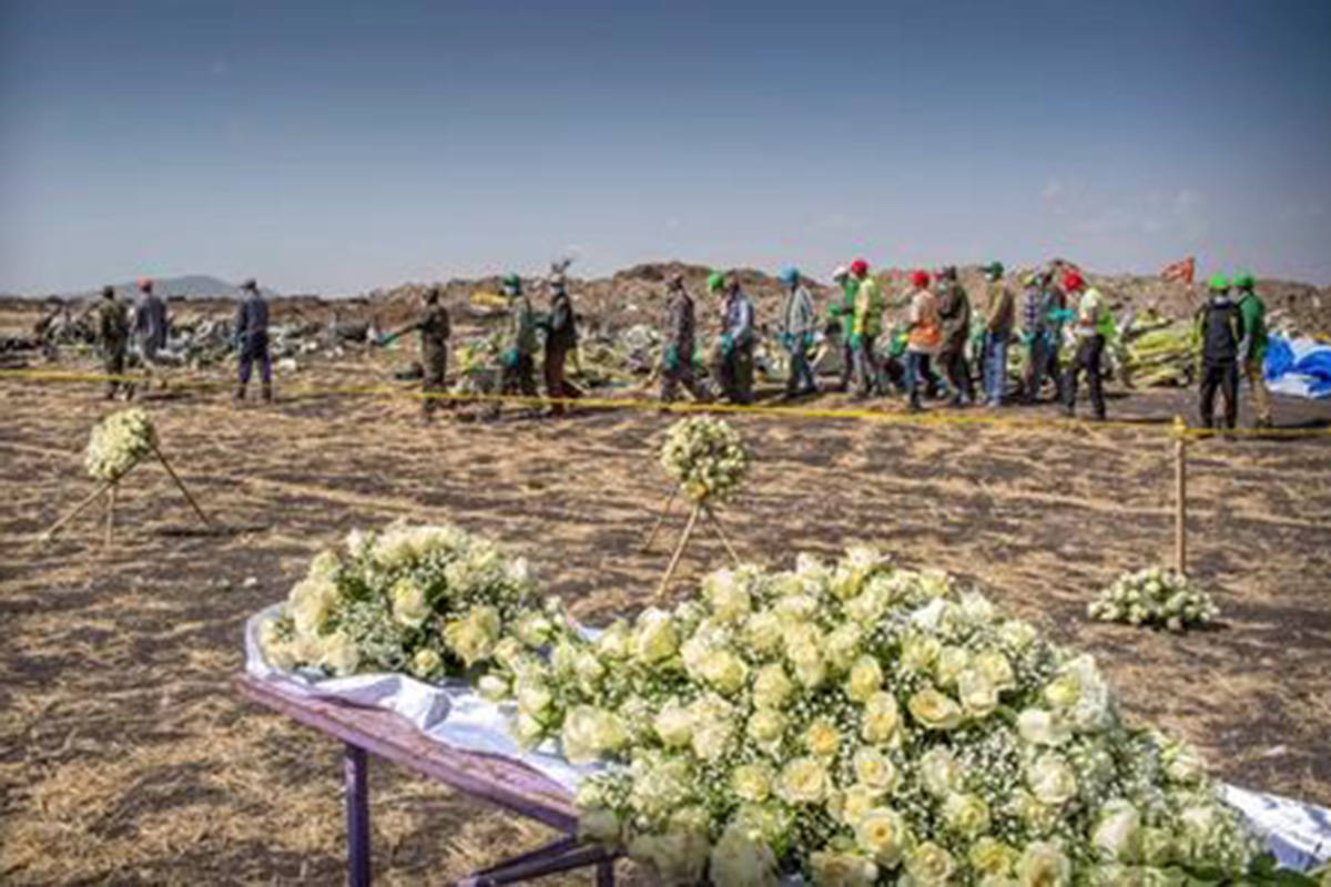 Workers walk past flowers laid at the scene where the Ethiopian Airlines Boeing 737 Max 8 crashed shortly after takeoff on Sunday killing all 157 on board, near Bishoftu, or Debre Zeit, south of Addis Ababa, in Ethiopia Wednesday, March 13, 2019. THE CANADIAN PRESS/AP-Mulugeta Ayene