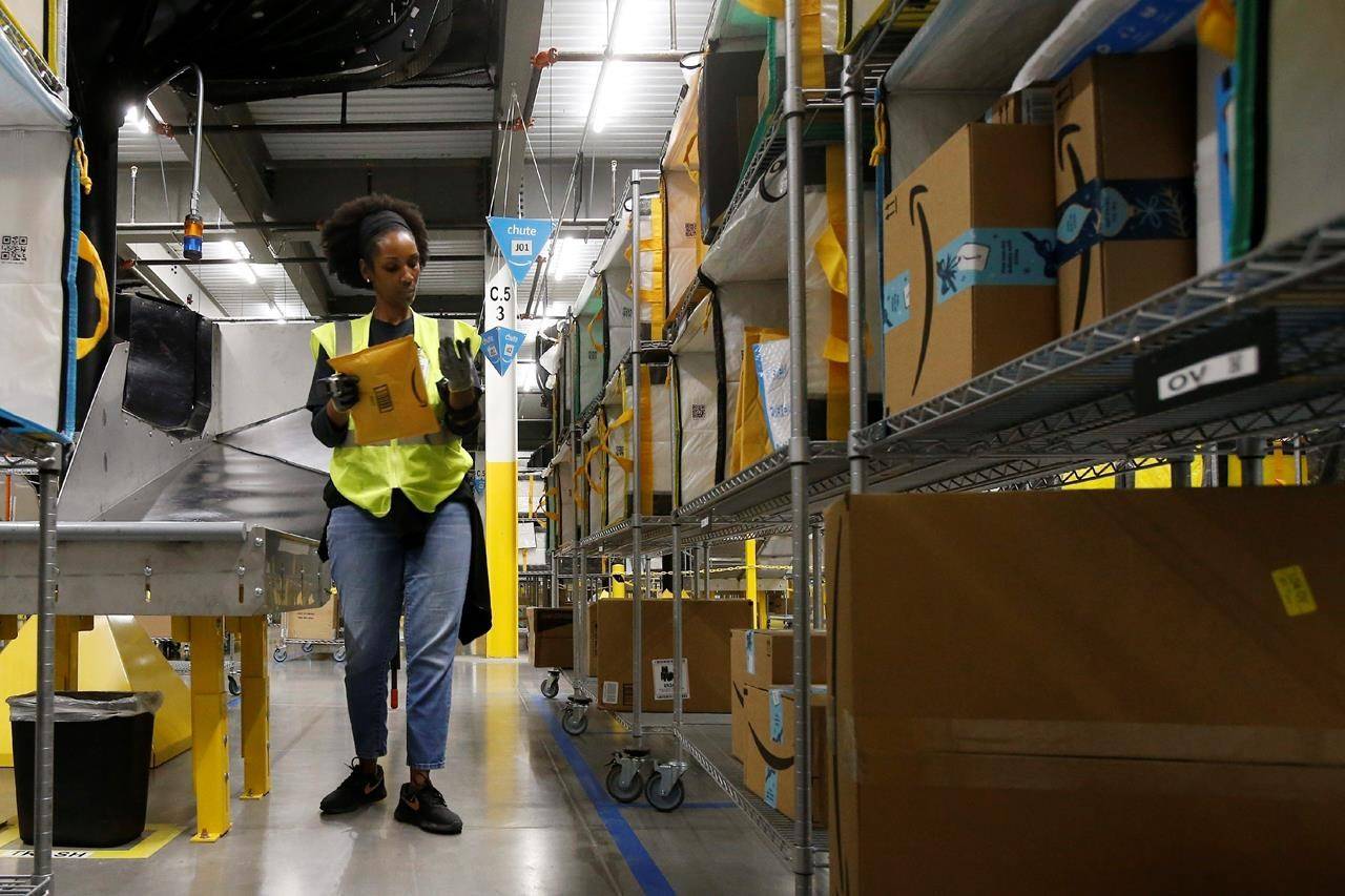 FILE - In this Dec. 17, 2019, file photo, Tahsha Sydnor stows packages into special containers after Amazon robots deliver separated packages by zip code at an Amazon warehouse facility in Goodyear, Ariz. On Monday, March 16, 2020, Amazon said that it needs to hire 100,000 people across the U.S. to keep up with a crush of orders as the coronavirus spreads and keeps more people at home, shopping online. (AP Photo/Ross D. Franklin, File)