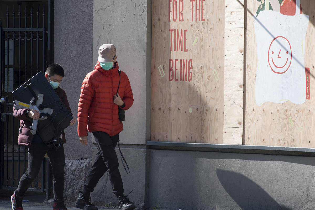 Two men wearing protective face masks as they walk past boarded up shops in downtown Vancouver, Monday, April 6, 2020. THE CANADIAN PRESS/Jonathan Hayward