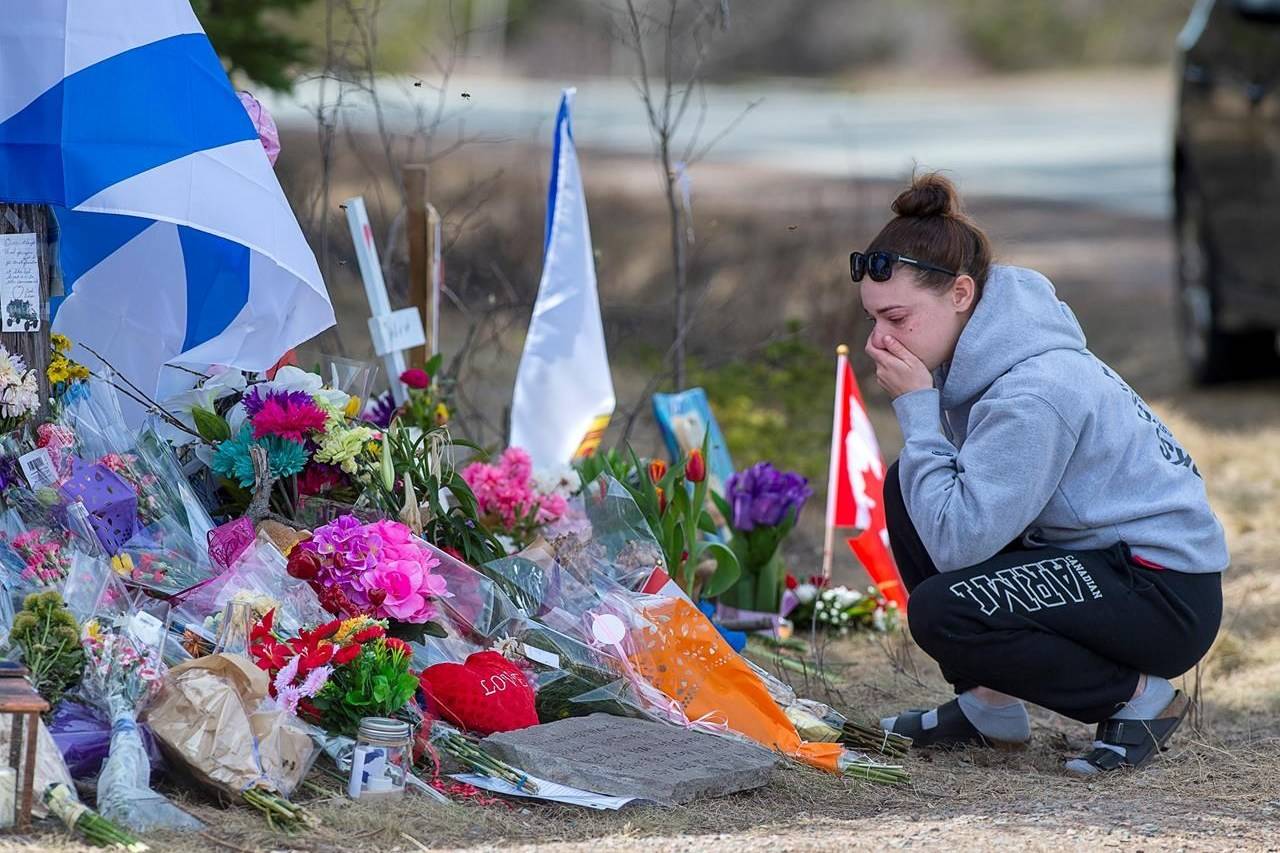 A woman pays her respects at a roadside memorial on Portapique Road in Portapique, N.S. on Friday, April 24, 2020. At least 22 people are dead after a man, who at one point wore a police uniform and drove a mock-up cruiser, went on a murder rampage in Portapique and several other Nova Scotia communities. THE CANADIAN PRESS/Andrew Vaughan
