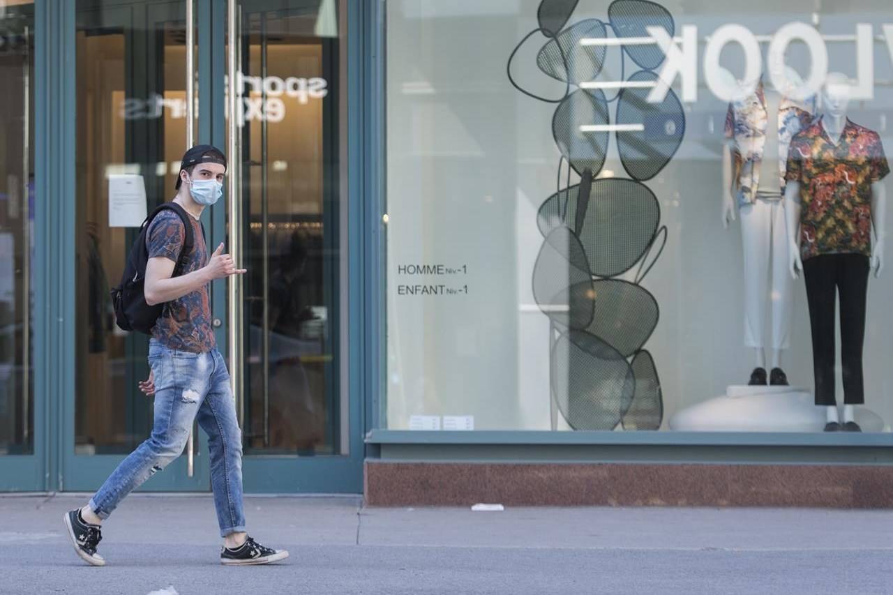 A man wearing a face mask gestures as he walks by a store on Sainte-Catherine street in Montreal, Monday, May 18, 2020. Shopping for clothes used to be a relatively simple process three months ago: walk into a store, try on a number of items, buy what you want, leave the rest. THE CANADIAN PRESS/Graham Hughes