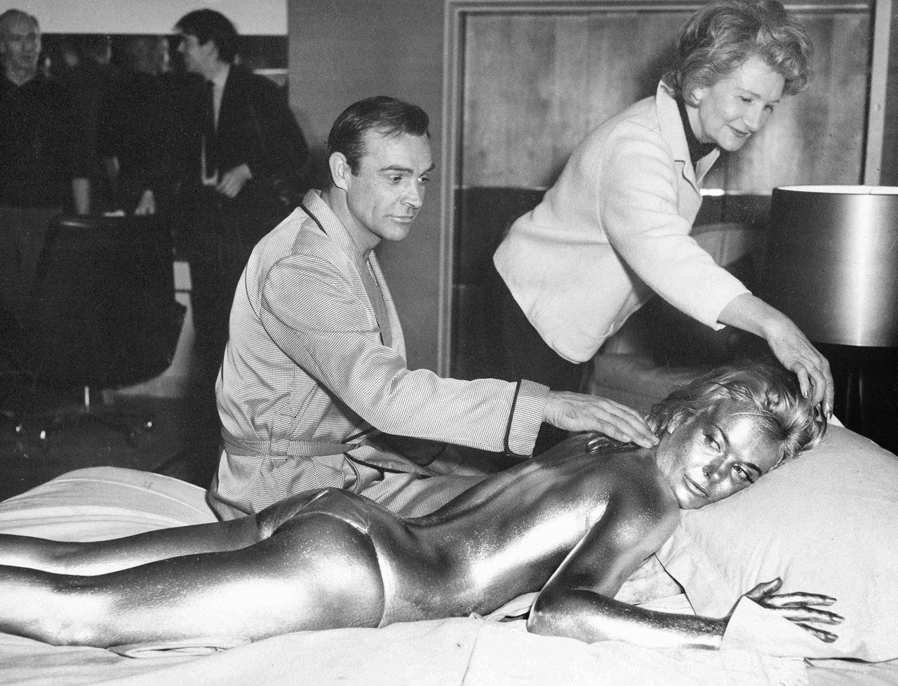 FILE - In this file photo dated April 20, 1964, James Bond, alias, Sean Connery, finds himself in a sticky situation with actress Shirley Eaton at Pinewood Studios, near London. Miss Eaton was given a liberal coating of gold paint for a scene in the latest Bond thriller “Goldfinger,” with unidentified woman at top. Scottish actor Sean Connery, considered by many to have been the best James Bond, has died aged 90, according to an announcement from his family. (AP Photo/Victor Boynton)