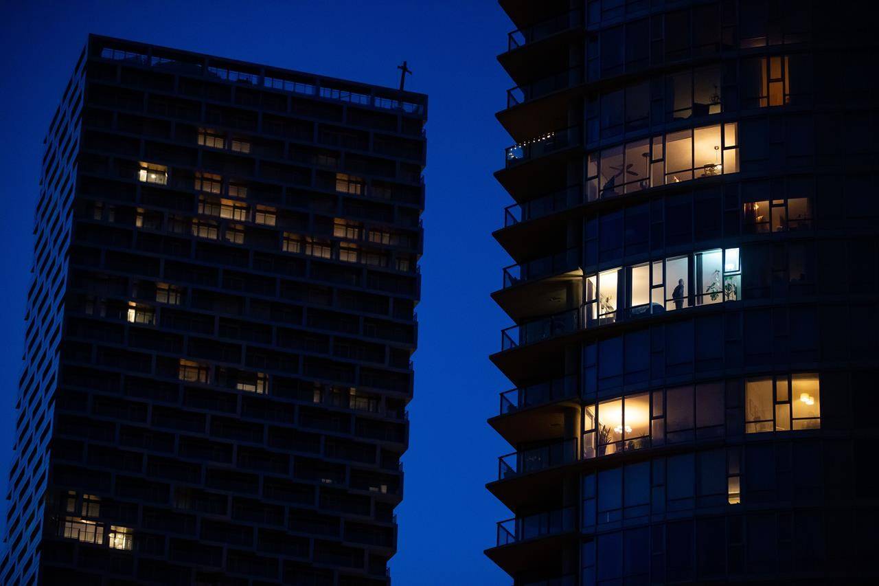 A man stands in the window of an upper floor condo in Vancouver on March 24, 2020. THE CANADIAN PRESS/Darryl Dyck