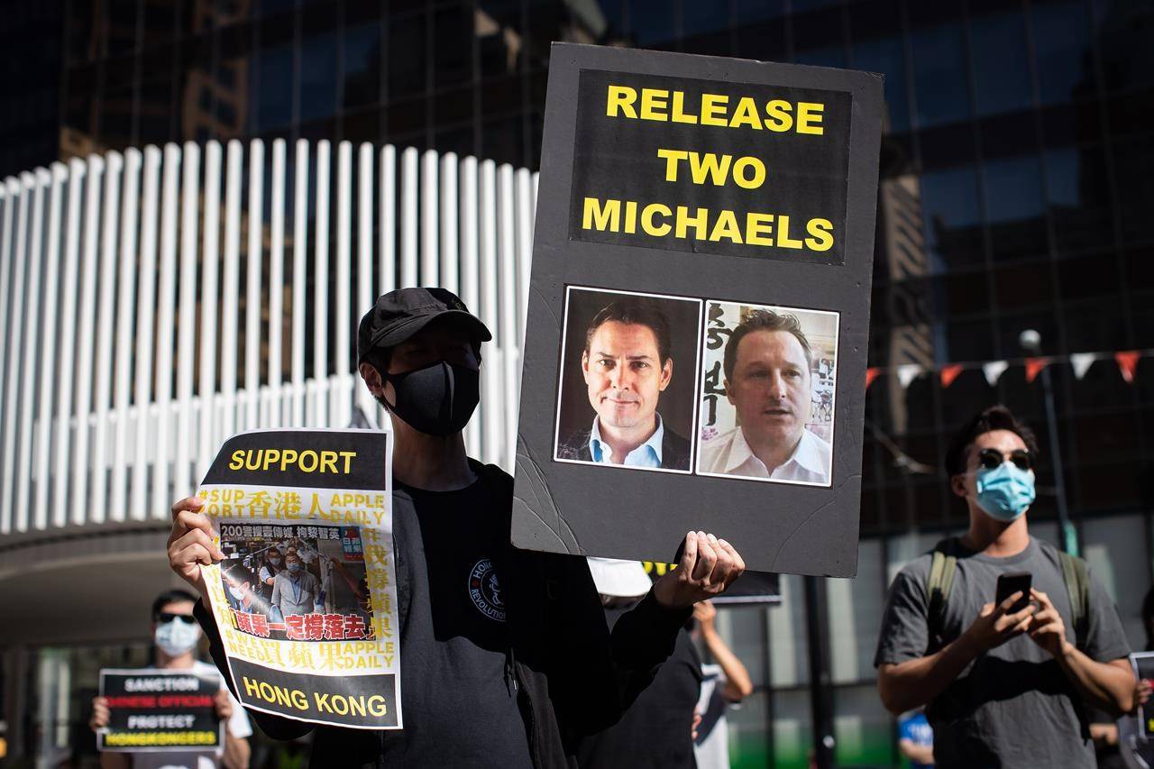 A person holds a sign with photographs of Michael Kovrig and Michael Spavor, who have been detained in China since December, 2018, as people gather for a rally in Vancouver, B.C., Sunday, Aug. 16, 2020. China is defending the way it has handled the cases of two Canadians who have been detained in the country for more than two years. THE CANADIAN PRESS/Darryl Dyck