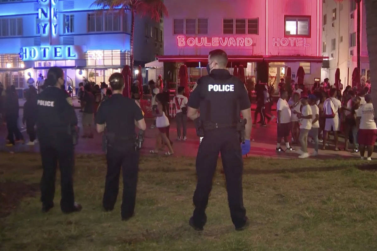 In this image taken from video, police officers stand guard Saturday evening, March 20, 2021, as crowds descend on South Beach in Miami. After days of partying and confrontations between police and large crowds, Miami Beach officials have ordered an emergency curfew. (WPLG via AP)