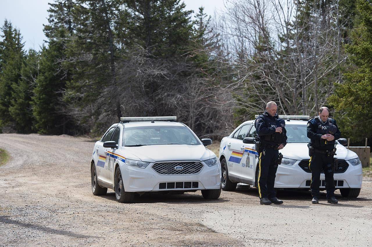 Two RCMP officers observe a moment of silence to honour slain Const. Heidi Stevenson and the other 21 victims of the mass killings at a checkpoint on Portapique Road in Portapique, N.S. on Friday, April 24, 2020. THE CANADIAN PRESS/Andrew Vaughan