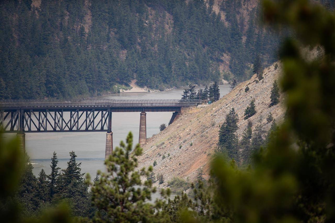 A rail bridge spans the Fraser River as a wildfire burns in Lytton, B.C., on Friday, July 2, 2021. THE CANADIAN PRESS/Darryl Dyck
