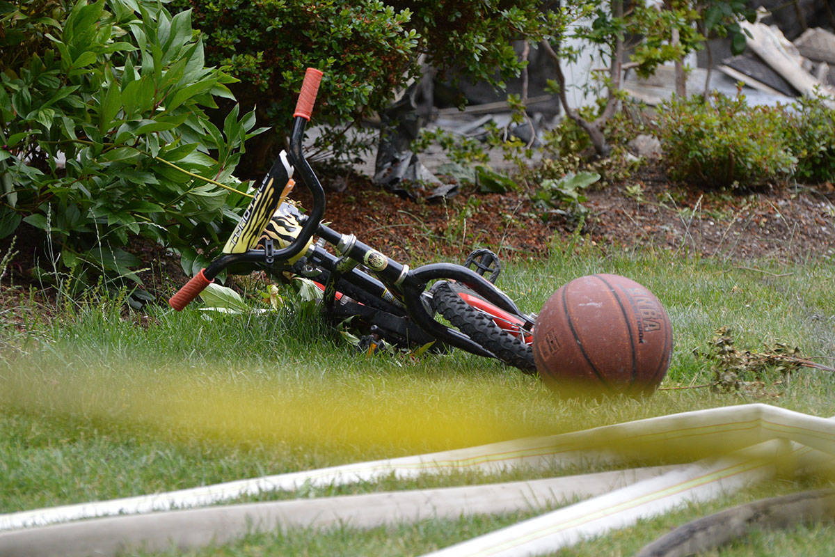 A child-sized bicycle and basketball rest behind police tape after a house fire in Surrey. Police are investigating after a five-year-old child was found dead. (Aaron Hinks photo)