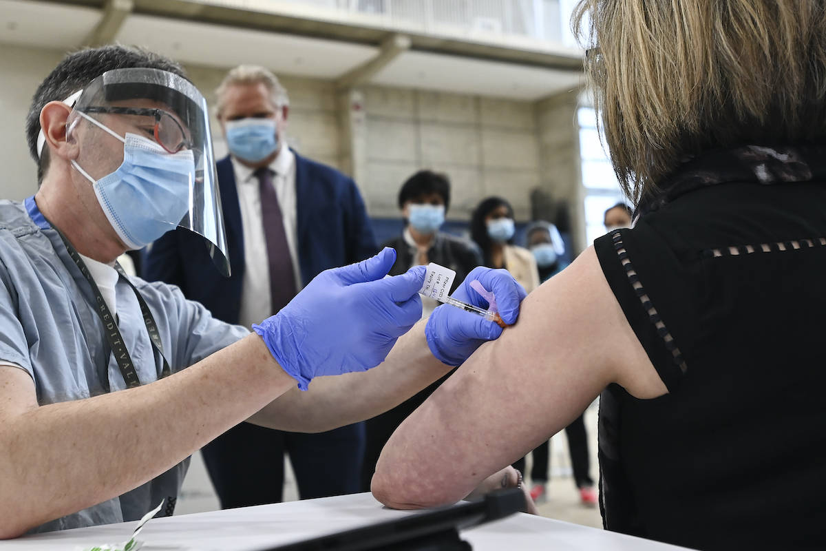Ontario Premier Doug Ford, centre, watches Dr. Vitaly Bard administer the coronavirus vaccine to nurse Mary Glenen-Calder as he tours a mass COVID-19 vaccination clinic for Peel Region during the COVID-19 pandemic in Mississauga, Ont., on Monday, March 1, 2021. THE CANADIAN PRESS/Nathan Denette