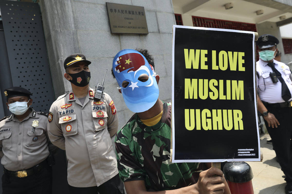 A Muslim student wearing a mask with the colors of the pro-independence East Turkistan flag, holds a poster during a rally outside the Chinese Embassy in Jakarta, Indonesia, Thursday, March 25, 2021. About a dozen of students staged the rally calling to an end to alleged oppression against Muslim Uyghur ethnic minority in China’s region of Xinjiang. (AP Photo/Dita Alangkara)