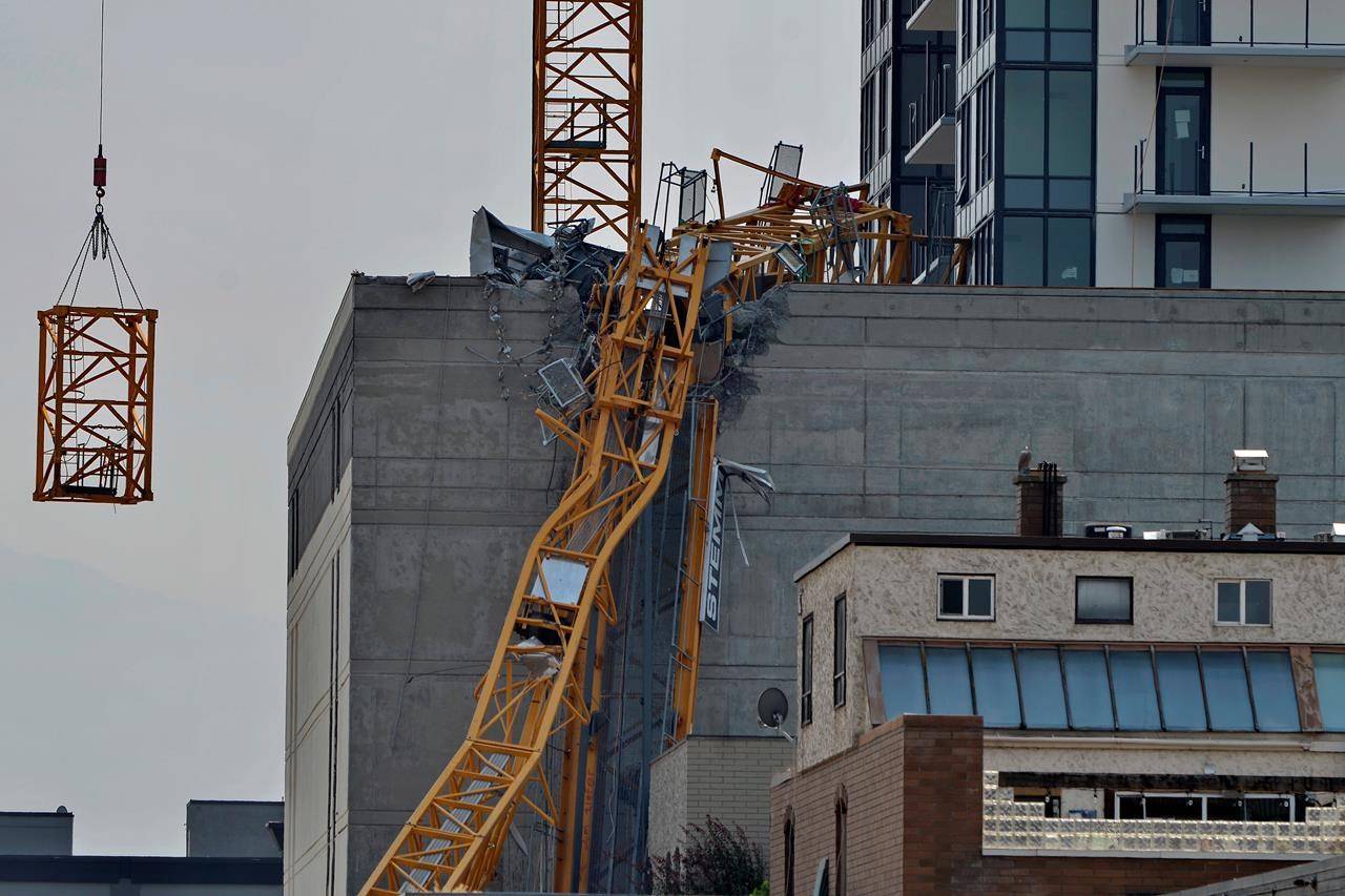 A section (left) of the vertical column of a construction crane is lowered past the mangled section of the fallen boom in Kelowna, B.C., Wednesday, July 14, 2021, following a fatal collapse of the crane on Monday. THE CANADIAN PRESS/Desmond Murray