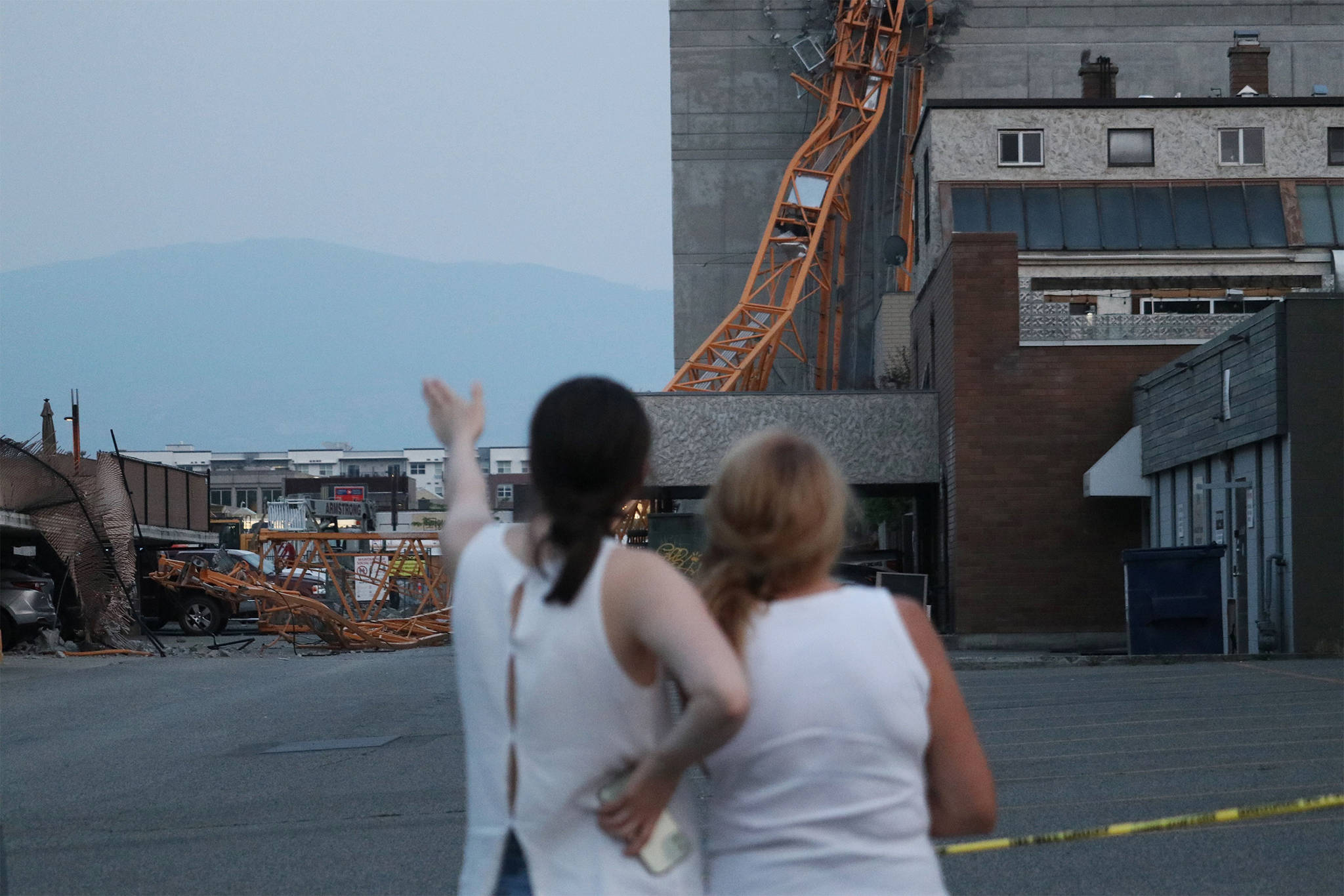 Two women look at the wreckage on the morning of Tuesday, July 13, after a crane collapsed in downtown Kelowna the previous day. (Aaron Hemens/Capital News)