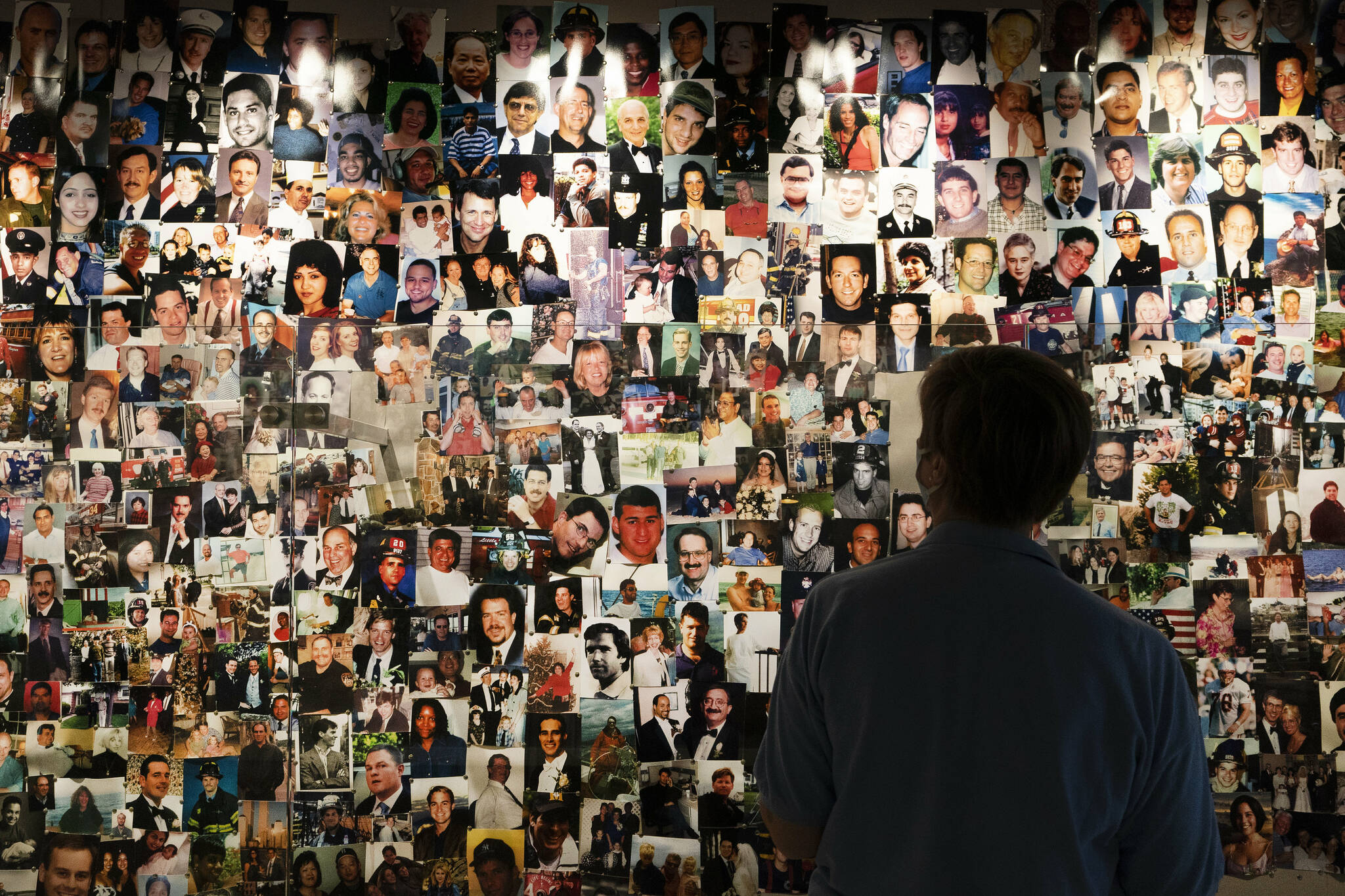 Désirée Bouchat, a survivor of the 9/11 attacks on the World Trade Center, looks at photos of those who perished, in a display at the 9/11 Tribute Museum, Friday, Aug. 6, 2021, in New York. While Sept. 11 was a day of carnage, it also was a story of survival: Nearly 3,000 people were killed, but an estimated 33,000 or more people evacuated the World Trade Center and Pentagon. (AP Photo/Mark Lennihan)
