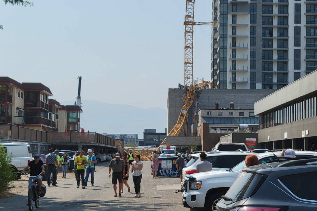 Several spectators look at the wreckage after a crane collapsed at a downtown Kelowna construction site on the morning of July 12, 2021. (Michael Rodriguez/Capital News)