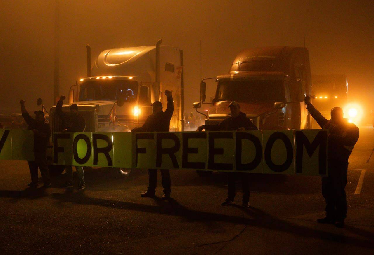 Truckers and supporters raise their fists and hold a banner before a cross-country convoy destined for Ottawa to protest a federal vaccine mandate for truckers departed in Delta, B.C. on Sunday, January 23, 2022. THE CANADIAN PRESS/Darryl Dyck