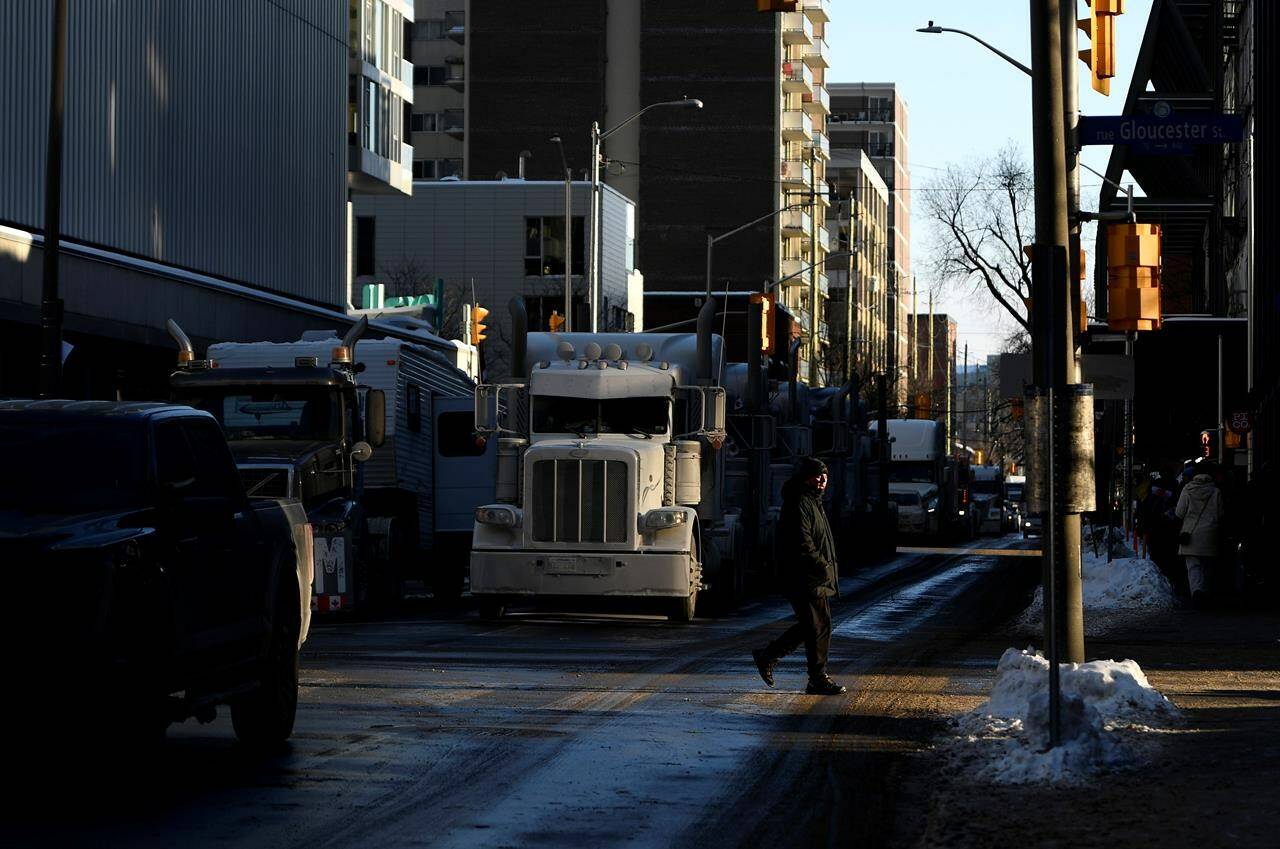 A person walks in a beam of afternoon sunlight as trucks are parked on Metcalfe Street part of a rally against COVID-19 restrictions, which began as a cross-country convoy protesting a federal vaccine mandate for truckers, which continues throughout downtown Ottawa, on Monday, Jan. 31, 2022. THE CANADIAN PRESS/Justin Tang