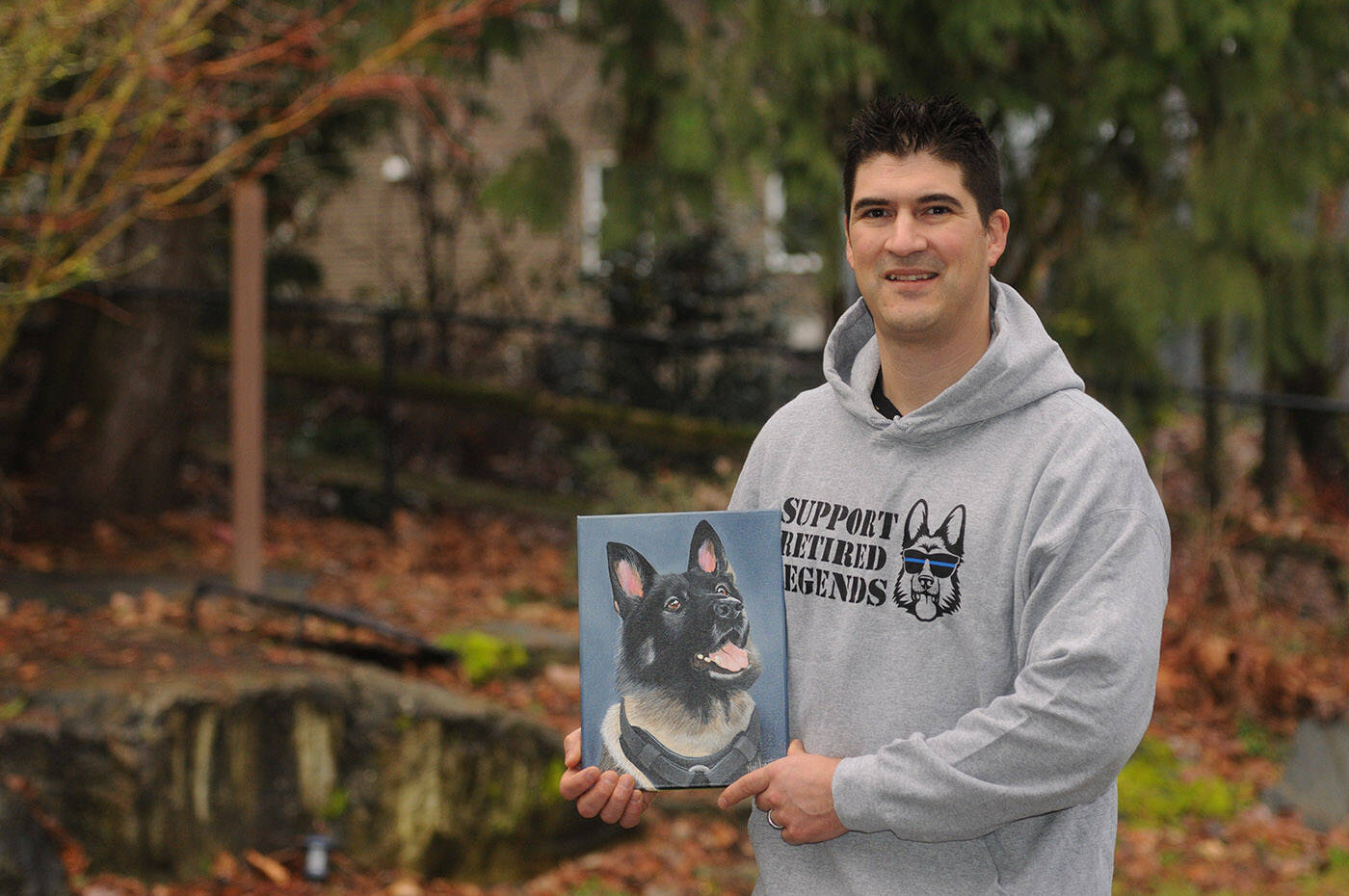 Const. Aaron Courtney hold a portrait of his late police dog Koda at his home in Chilliwack on Feb. 17, 2022. He, along with partner Sgt. Jason Martens and their wives started Support Retired Legends, a business which raises money for a charity called Ned’s Wish which provides financial support to help pay for the medical bills of retired service dogs. (Jenna Hauck/ Chilliwack Progress)