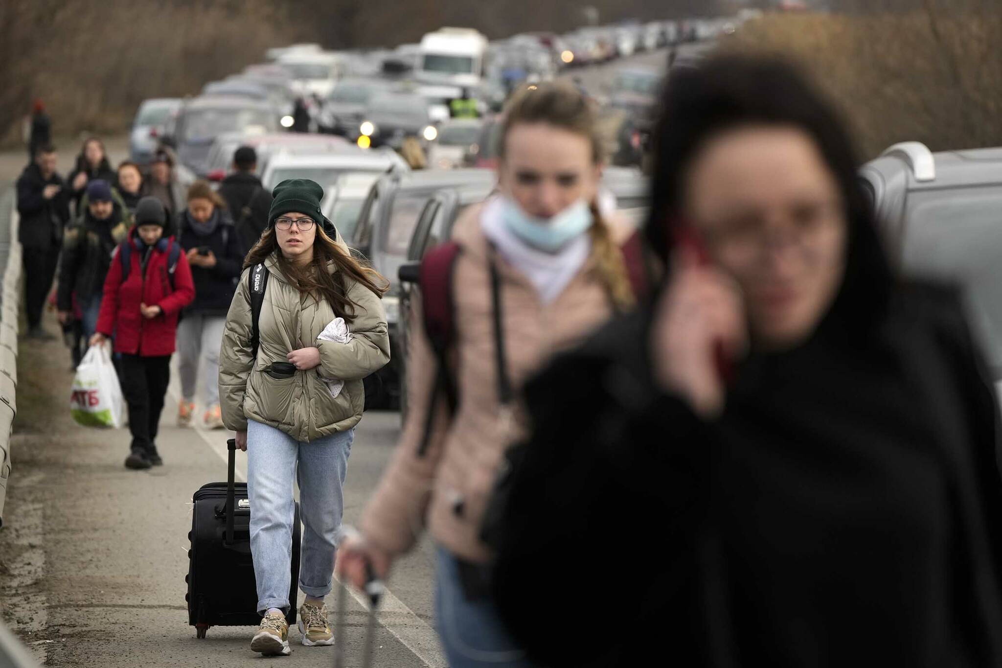 Ukrainian refugees walk along vehicles lining-up to cross the border from Ukraine into Moldova, at Mayaky-Udobne crossing border point near Udobne, Ukraine, Saturday, Feb. 26, 2022. (AP Photo/Sergei Grits)