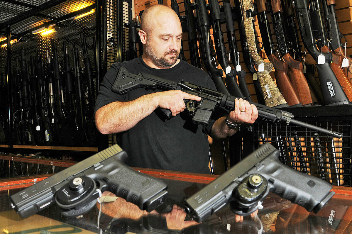 Craig Jones, co-owner of Wanstalls, holds an AR15 variant, when they were legal to sell, with two Glock 22’s in the foreground. (THE NEWS/files)