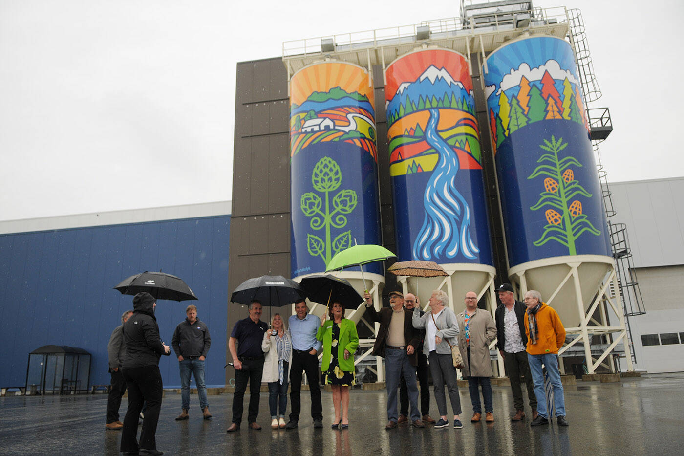 Members of the public art advisory committee line up for a photo in front of ‘Gifts of Nature,’ a public art piece installed on silos outside the Molson Coors Fraser Valley Brewery and unveiled on Thursday, June 9, 2022. The piece was designed by Chilliwack artist Silvana Kulyk. (Jenna Hauck/ Chilliwack Progress)