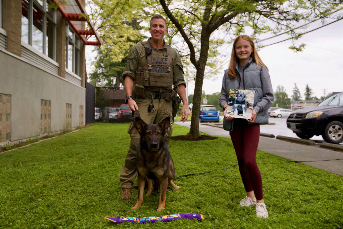 RCMP dog handler Cpl. Dave Lewis and his police dog Halla stand with Josslyn Jeary holding a photo of Rigby on June 15. Jeary was one of 13 winners of the RCMP’s national Name the Puppy Contest held each year to name the upcoming class of police dogs. (Justin Samanski-Langille/News Staff)