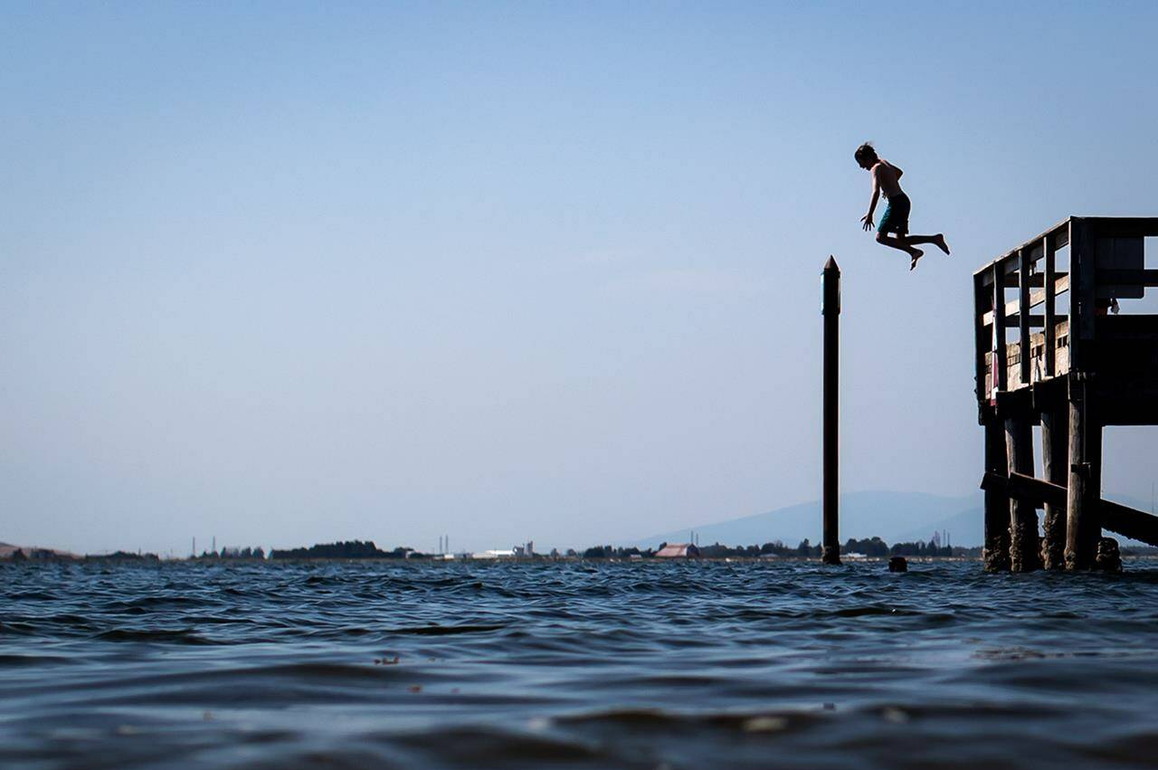 A young boy is silhouetted as he jumps off the pier at Crescent Beach into Boundary Bay, in Surrey, B.C., Tuesday, July 6, 2021. THE CANADIAN PRESS/Darryl Dyck