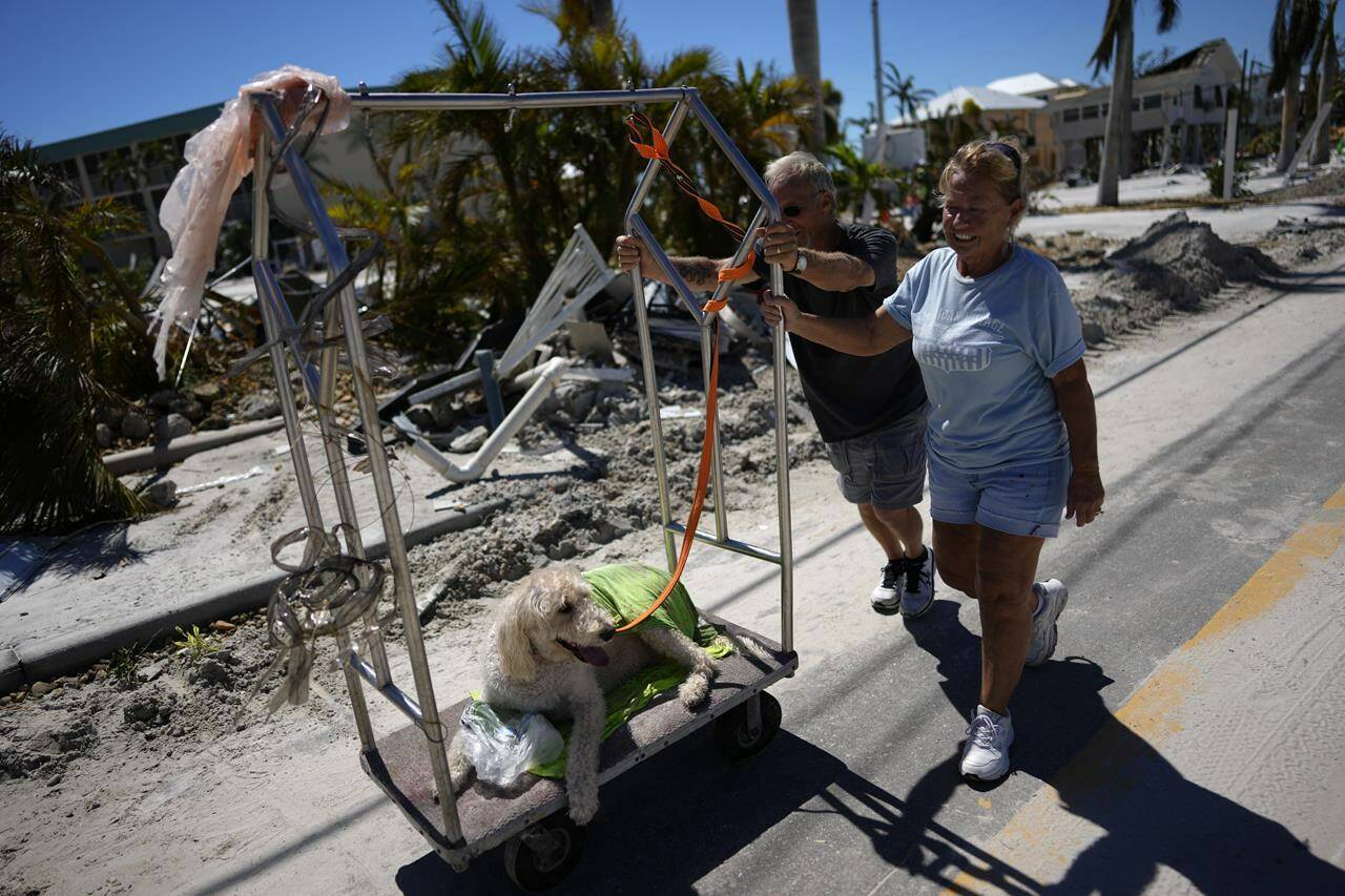 Debbie and Lou Evans push their dog Brody on a hotel luggage cart they found amidst the wreckage, as they come to check on their home, two days after the passage of Hurricane Ian, in Fort Myers Beach, Fla., Friday, Sept. 30, 2022. (AP Photo/Rebecca Blackwell)