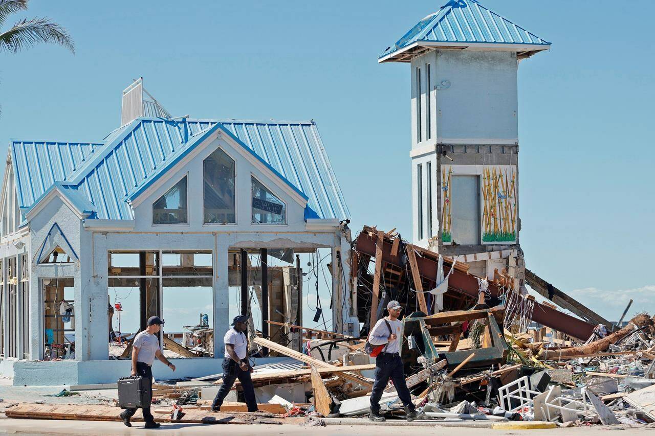 Emergency workers walk past the remains of a clothing store, blown out by Hurricane Ian, in the Times Square area near the Lynn Hall Pier on the island of Fort Myers Beach, Fla., Friday, Sept. 30, 2022. Hurricane Ian made landfall Wednesday, Sept. 28, 2022, as a Category 4 hurricane on the southwest coast of Florida. (Amy Beth Bennett/South Florida Sun-Sentinel via AP)