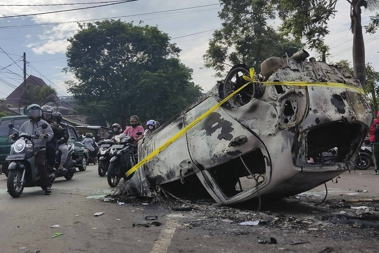 Motorists ride past the wreckage of a car burned during a clash between supporters of two soccer teams, outside Kanjuruhan Stadium in Malang, East Java, Indonesia, Sunday, Oct. 2, 2022. Panic following police actions at the stadium left over 100 dead, mostly trampled to death, police said Sunday. (AP Photo/Hendra Permana)