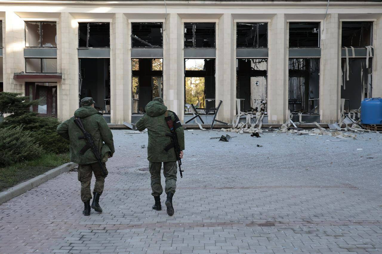 Two armed servicemen walk at the site of a damaged administrative building after shelling in Donetsk, the capital of Donetsk People's Republic, eastern in Ukraine, Sunday, Oct. 16, 2022. Russian media reports say the mayor’s office in a key eastern Ukrainian city controlled by pro-Kremlin separatists has been struck by rockets. There were no immediate reports of casualties in the Sunday morning attack. (AP Photo/Alexei Alexandrov)