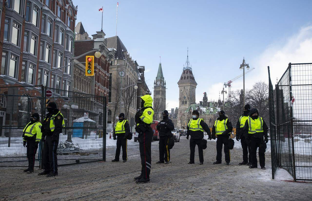 The Peace Tower is seen behind police at a gate along Queen Street as they restrict access to the streets around Parliament Hill in Ottawa, Saturday, Feb. 19, 2022. The inquiry into the federal government’s use of the Emergencies Act during February’s “Freedom Convoy” protest in Ottawa continues today. THE CANADIAN PRESS/Justin Tang