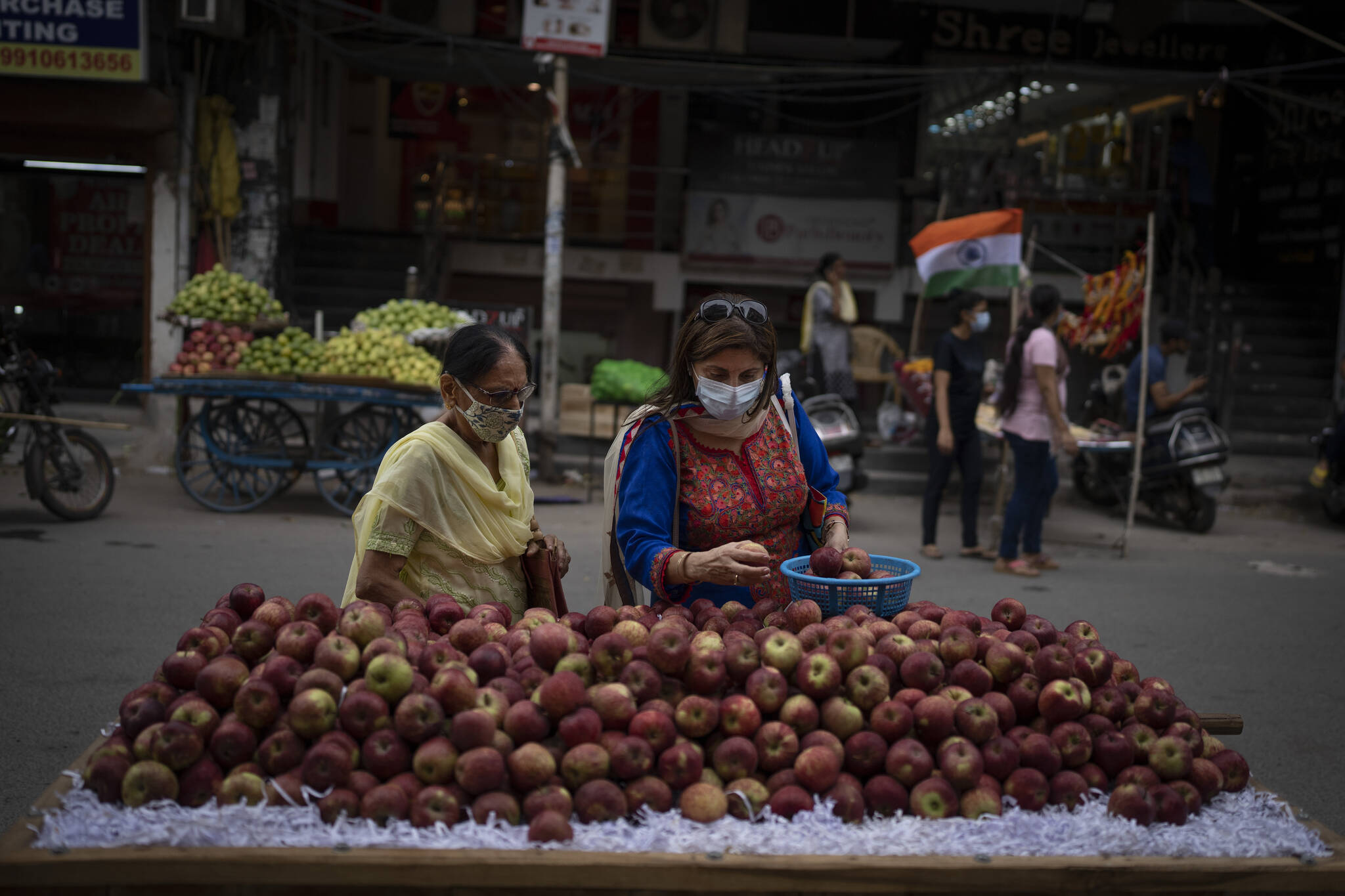 Women wearing masks as a precaution against the coronavirus buy apples from a roadside vendor in New Delhi, India, Thursday, Aug. 11, 2022. The Indian capital reintroduced public mask mandates on Thursday as COVID-19 cases continue to rise across the country. (AP Photo/Altaf Qadri)