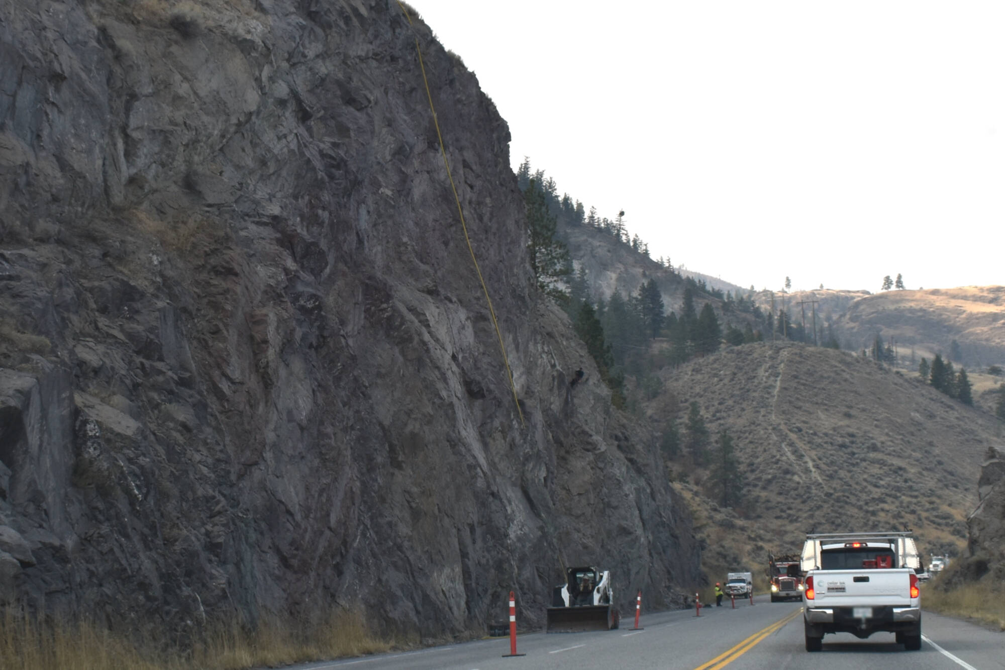 A worker scales the clifface while another in a skid-steer removes fallen rock from a section under work on Highway 97 between Kaleden and Penticton. (Brennan Phillips - Western News)