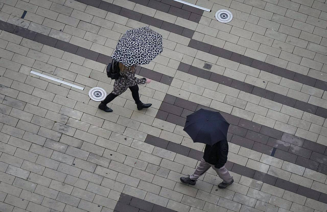 Pedestrians carry umbrellas as light rain falls in Surrey, B.C., on Friday, October 21, 2022. BC Hydro says electricity has been restored to most of its more than 100,000 customers blacked out during the first powerful storm of British Columbia’s late-arriving fall, but forecasters warn more foul weather is on the way. THE CANADIAN PRESS/Darryl Dyck