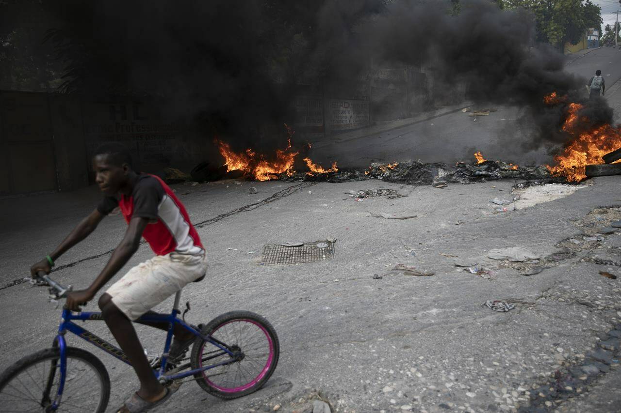 A man rides his bicycle a burning barricade during a protest over the death of journalist Romelo Vilsaint, in Port-au-Prince, Haiti, Sunday, Oct. 30, 2022. THE CANADIAN PRESS/AP-Odelyn Joseph