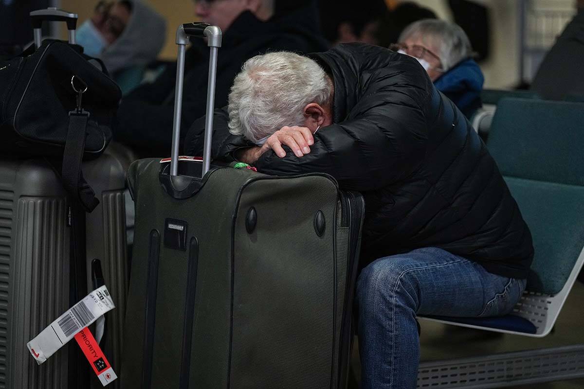 A man rests on his luggage at Vancouver International Airport after a snowstorm crippled operations leading to cancellations and major delays, in Richmond, B.C., on Tuesday, December 20, 2022. THE CANADIAN PRESS/Darryl Dyck