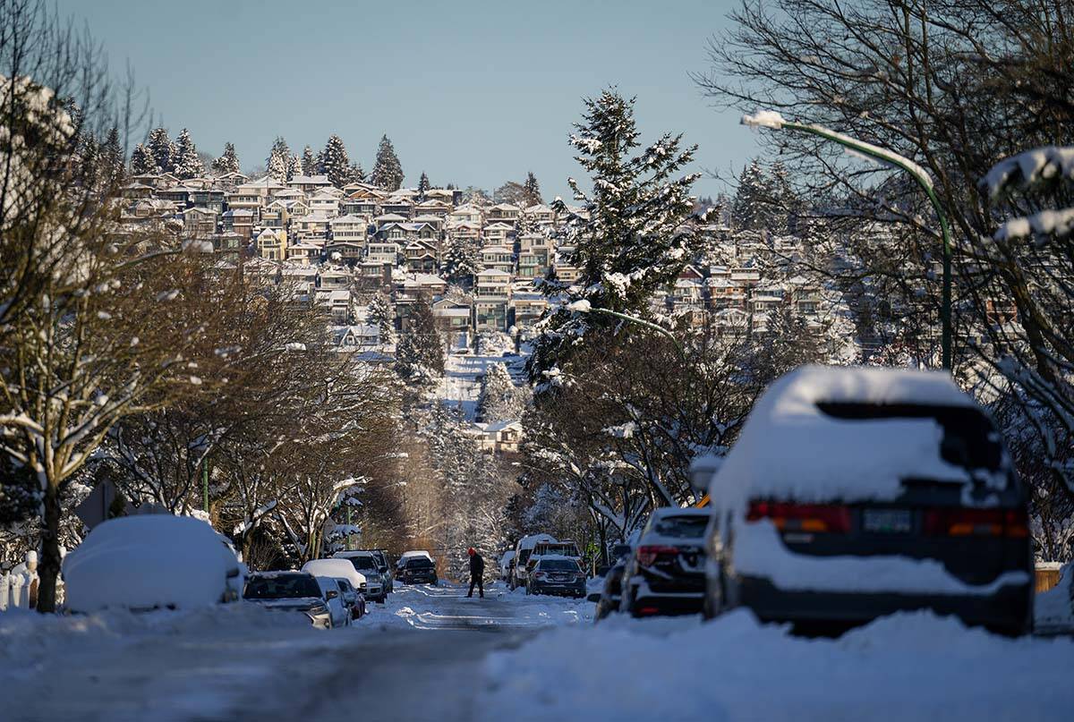 A person crosses a snow and ice covered road in Burnaby, B.C., on Wednesday, December 21, 2022. A snowstorm dumped more than 30 centimetres of snow in Metro Vancouver this week. THE CANADIAN PRESS/Darryl Dyck