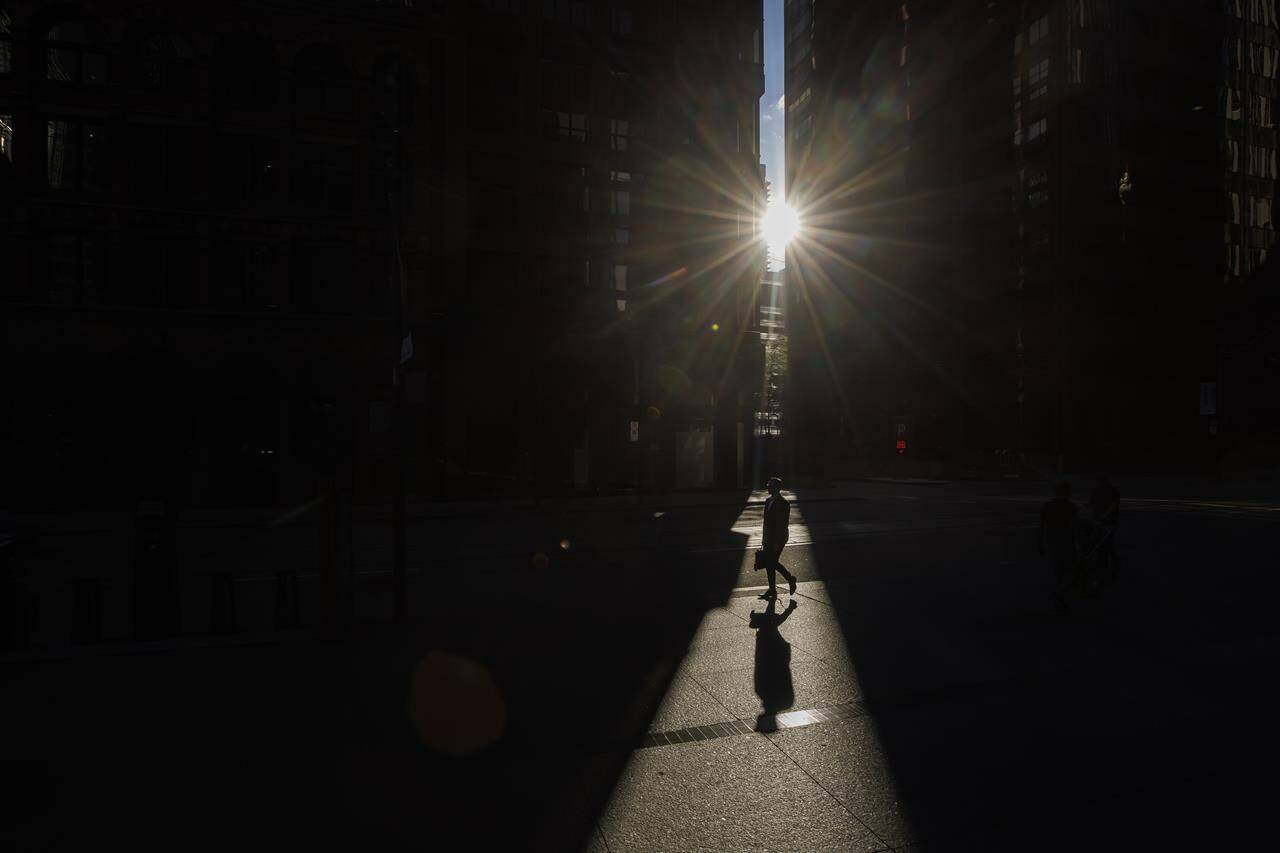 Pedestrians walk through a sliver of sunlight in the financial district in downtown Toronto on Wednesday July 6, 2022. THE CANADIAN PRESS/Cole Burston