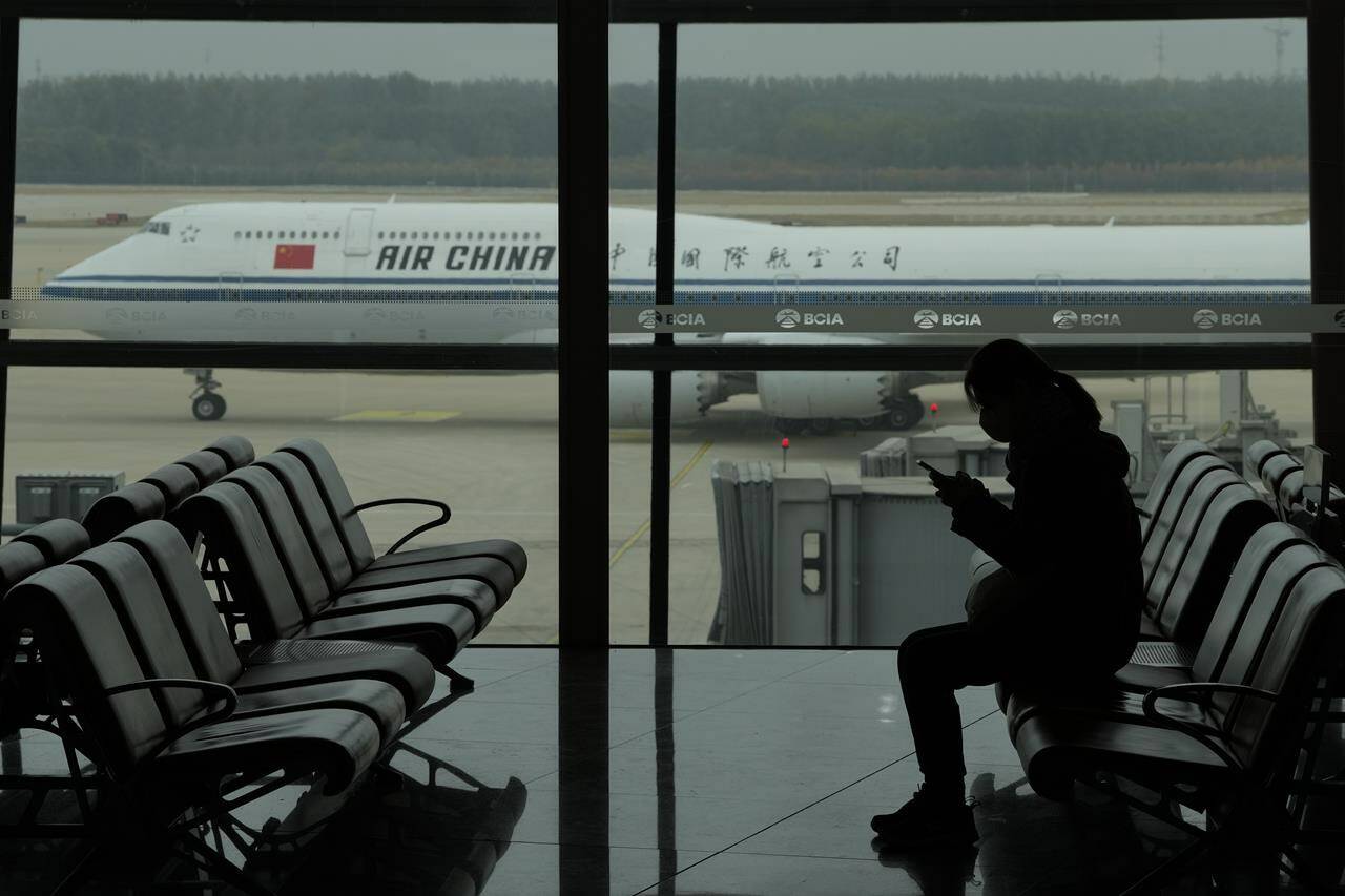 A passenger checks her phone as an Air China passenger jet taxi past at the Beijing Capital International airport in Beijing, Saturday, Oct. 29, 2022. China will drop a COVID-19 quarantine requirement for passengers arriving from abroad starting Jan. 8. The National Health Commission announced the change Monday, Dec. 26, 2022 as part of the latest easing of China’s once strict virus control measures. (AP Photo/Ng Han Guan)