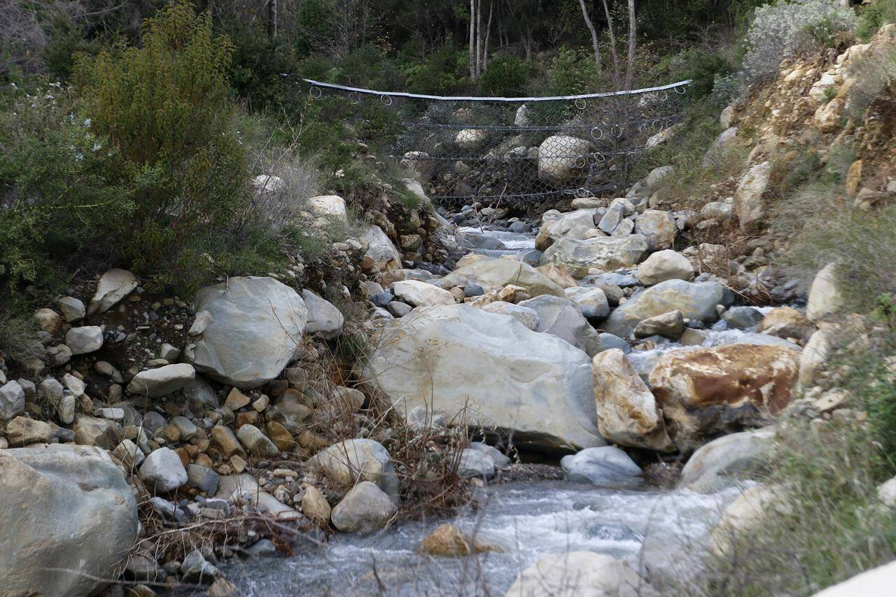 Netting made from mettle cables is visible above a creek in Montecito, Calif., on Thursday, Jan. 12, 2023. With climate change predicted to produce more severe weather, officials are scrambling to put in basins, nets and improve predictions of where landslides might occur to keep homes and people safe. (AP Photo/Ty O’Neil)