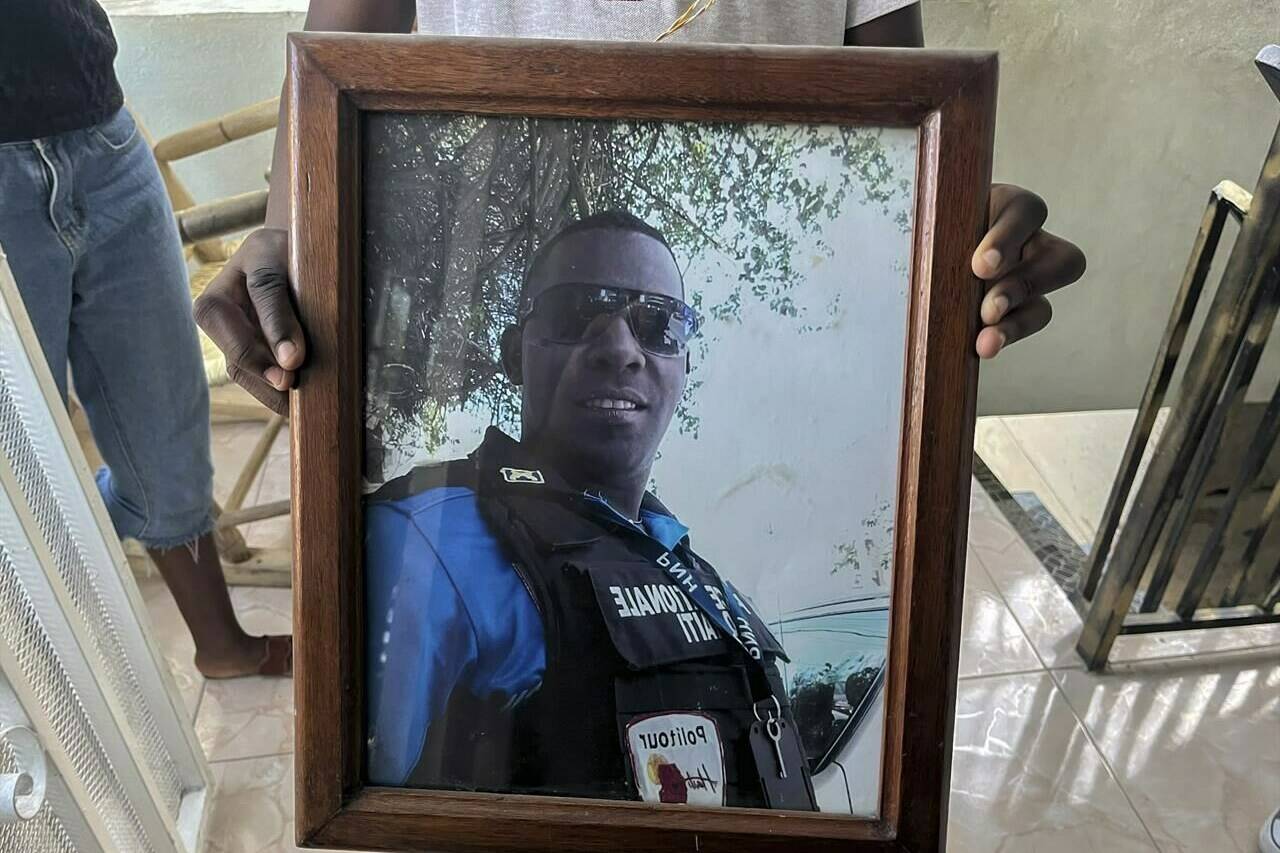 A photo of missing Haitian police Officer Ricken Staniclasse is held by his 11-year-old son at their home in Port-au-Prince, Haiti, Saturday, Jan. 21, 2023. One of Haiti’s gangs stormed a key part of the capital, Port-Au-Prince, and battled with police throughout the day, leaving at least three officers dead and another missing. (AP Photo/Megan Janetsky)