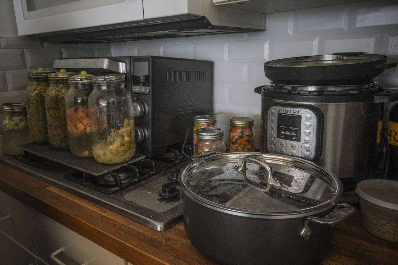 Jars of fermenting fruits and vegetables, left, sit on top of a retired gas stove replaced by an electric cooker, right, in Josh Spodek's Greenwich Village apartment kitchen, Tuesday Jan. 24, 2023, in New York. Spodek's efforts to go packaging-free changed his mindset and led him to experiment with living grid-free (AP Photo/Bebeto Matthews)