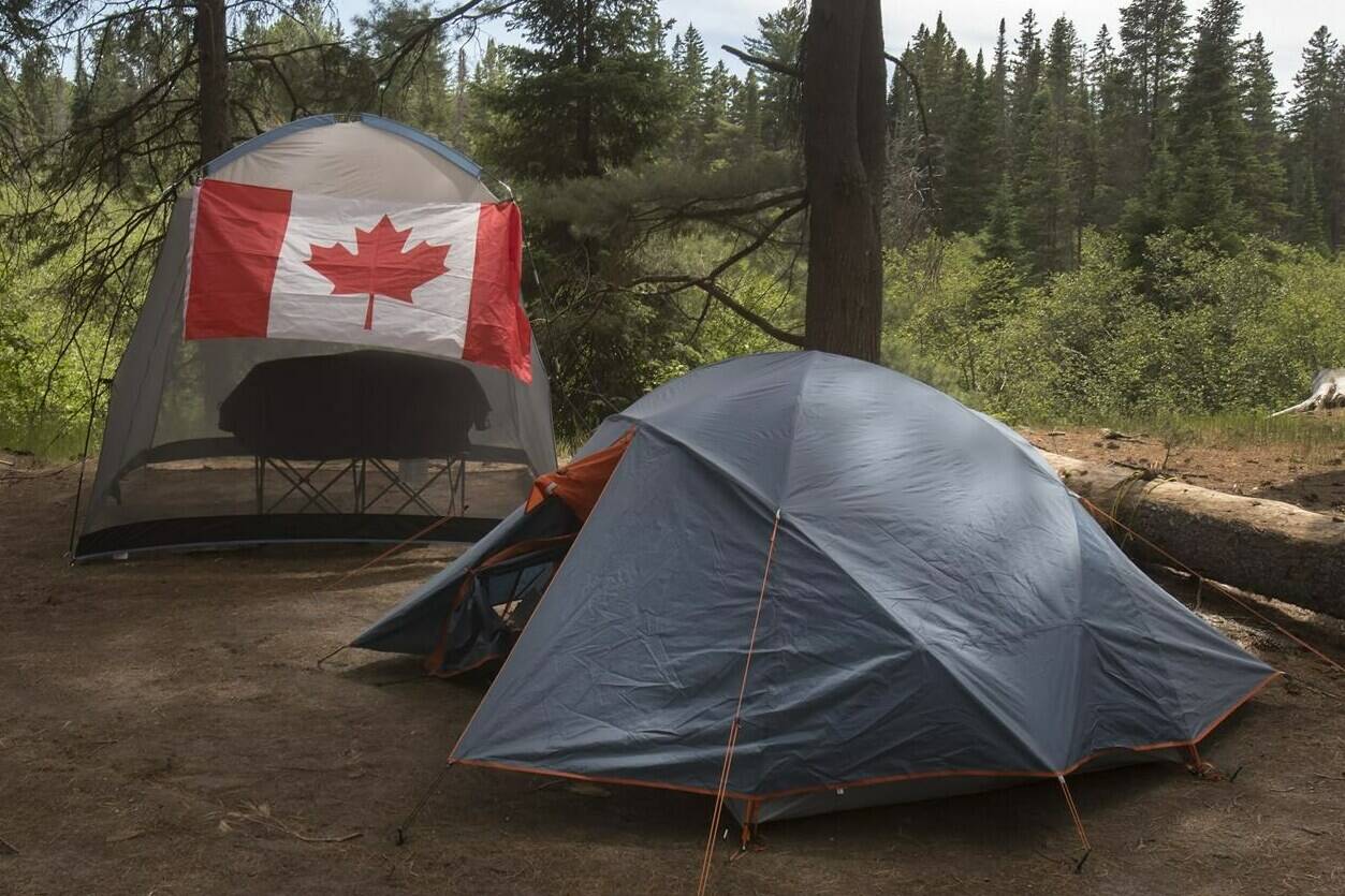 Campers with a Canadian flag flying on their camp site are shown in Algonquin Park on Saturday, June 12, 2021. Parks Canada says visitors will be able to start booking reservations for camping and other activities at its sites across the country in March. THE CANADIAN PRESS/Fred Thornhill