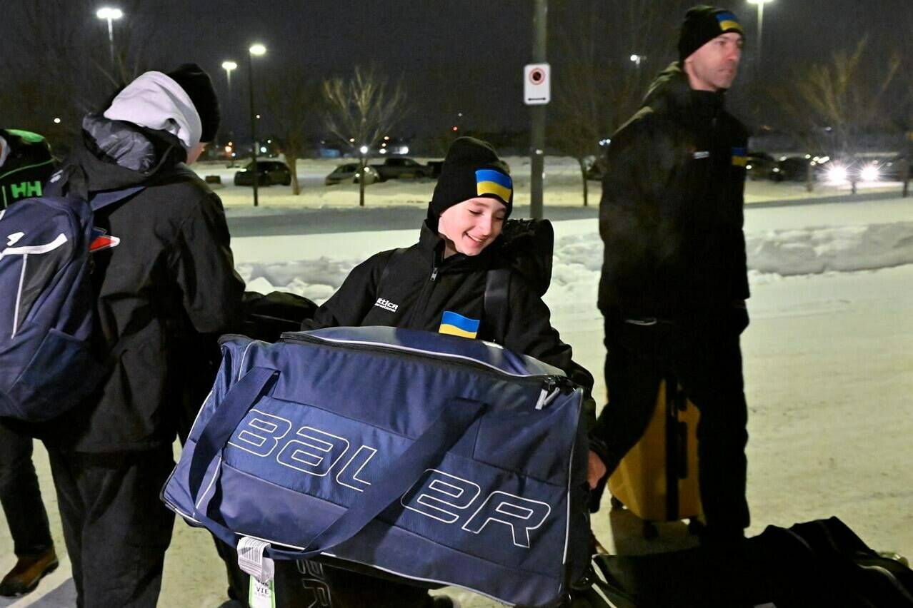 Ukrainian peewee hockey player Zahar Kovalenko carries his bag as head coach Evgheniy Pysarenko walks behind as they arrive, Wednesday, Feb. 1, 2023, at the Videotron Centre in Quebec City. The Ukraine team will compete at the Quebec international peewee tournament. THE CANADIAN PRESS/Jacques Boissinot