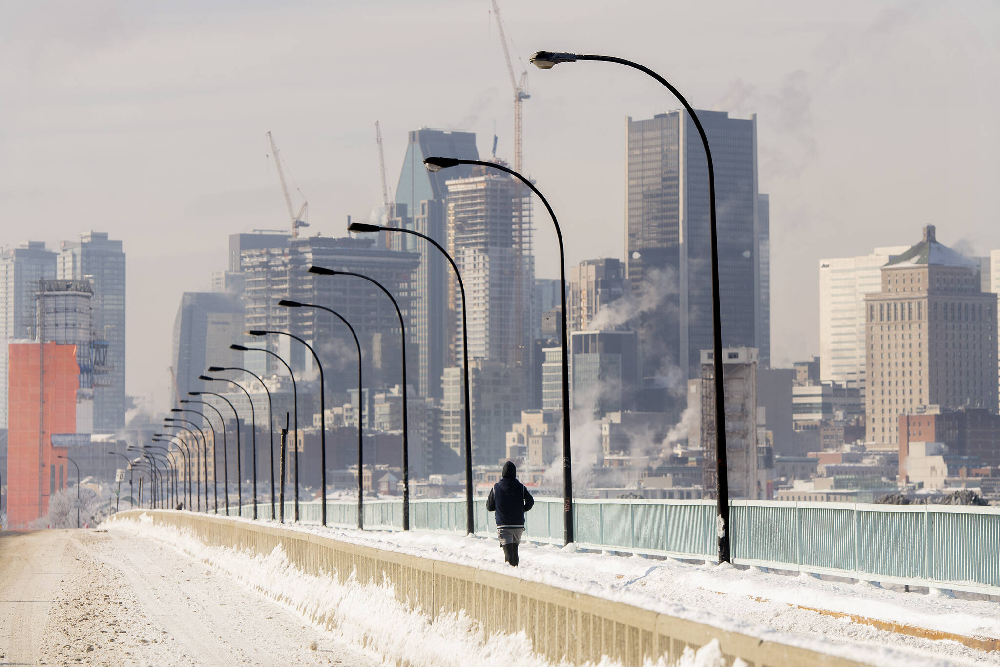 A person jogs next to a backdrop of the Montreal skyline as ice fog rises off the St. Lawerence River in Montreal, Saturday, Jan. 22, 2022. Environment Canada has issued an extreme cold warning for the region. THE CANADIAN PRESS/Graham Hughes