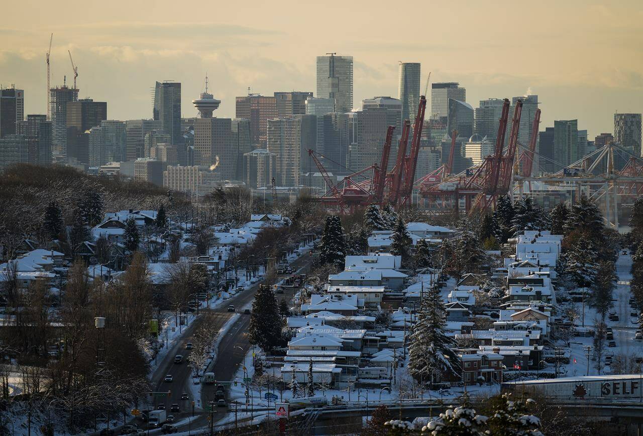 Houses are covered with snow as the downtown skyline is seen in the distance, in Vancouver, on Wednesday, December 21, 2022. The British Columbia Real Estate Association says the chill across the province’s real estate sector will drag on through 2023, but it calls for a strong rebound next year. THE CANADIAN PRESS/Darryl Dyck