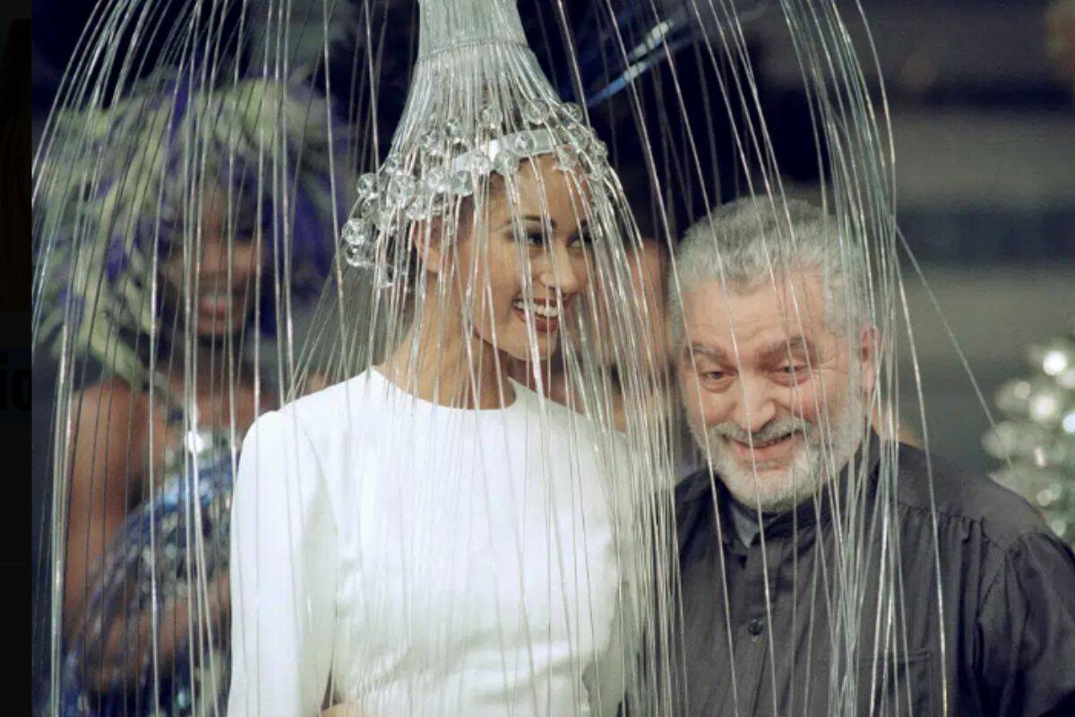 FILE - Spanish fashion designer Paco Rabanne poses with a model wearing a white dress with a metallic headpiece after presenting his 1992/93 fall-winter haute couture collection in Paris, France, on July 29, 1992. The Spanish-born pace-setting designer known for perfumes sold worldwide and his metallic, space-age fashions, has died, the group that owns his fashion house announced on its website Friday Feb.3, 2023. He was 88. (AP Photo/Laurent Rebours, File)