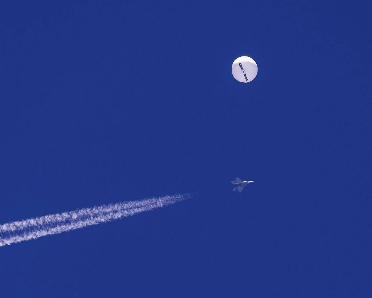 FILE - In this photo provided by Chad Fish, a large balloon drifts above the Atlantic Ocean, just off the coast of South Carolina, with a fighter jet and its contrail seen below it, Saturday, Feb. 4, 2023. A missile fired on Feb. 5 by a U.S. F-22 off the Carolina coast ended the days-long flight of what the Biden administration says was a surveillance operation that took the Chinese balloon near U.S. military sites. (Chad Fish via AP)