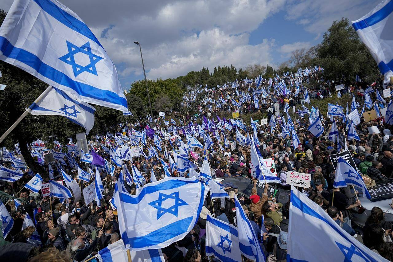 Israelis wave national flags during protest against plans by Prime Minister Benjamin Netanyahu’s new government to overhaul the judicial system, outside the Knesset, Israel’s parliament, in Jerusalem, Monday, Feb. 13, 2023. Thousands of Israelis protested outside the country’s parliament on Monday ahead of a preliminary vote on a bill that would give politicians greater power over appointing judges, part of a judicial overhaul proposed by Prime Minister Benjamin Netanyahu’s government. (AP Photo/Ohad Zwigenberg)