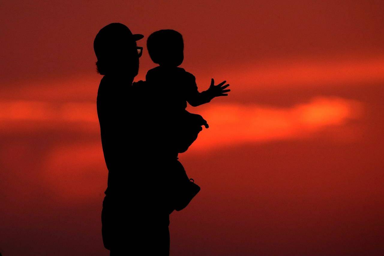 A British Columbia advocacy organization says child poverty decreased in the province in 2020 due to government benefits launched in response to the COVID-19 pandemic, but the progress may be wiped out by rising living costs. A silhouette against the sky of a man holding a child in Kansas City, Mo., Friday, June 26, 2020. THE CANADIAN PRESS/AP-Charlie Riedel